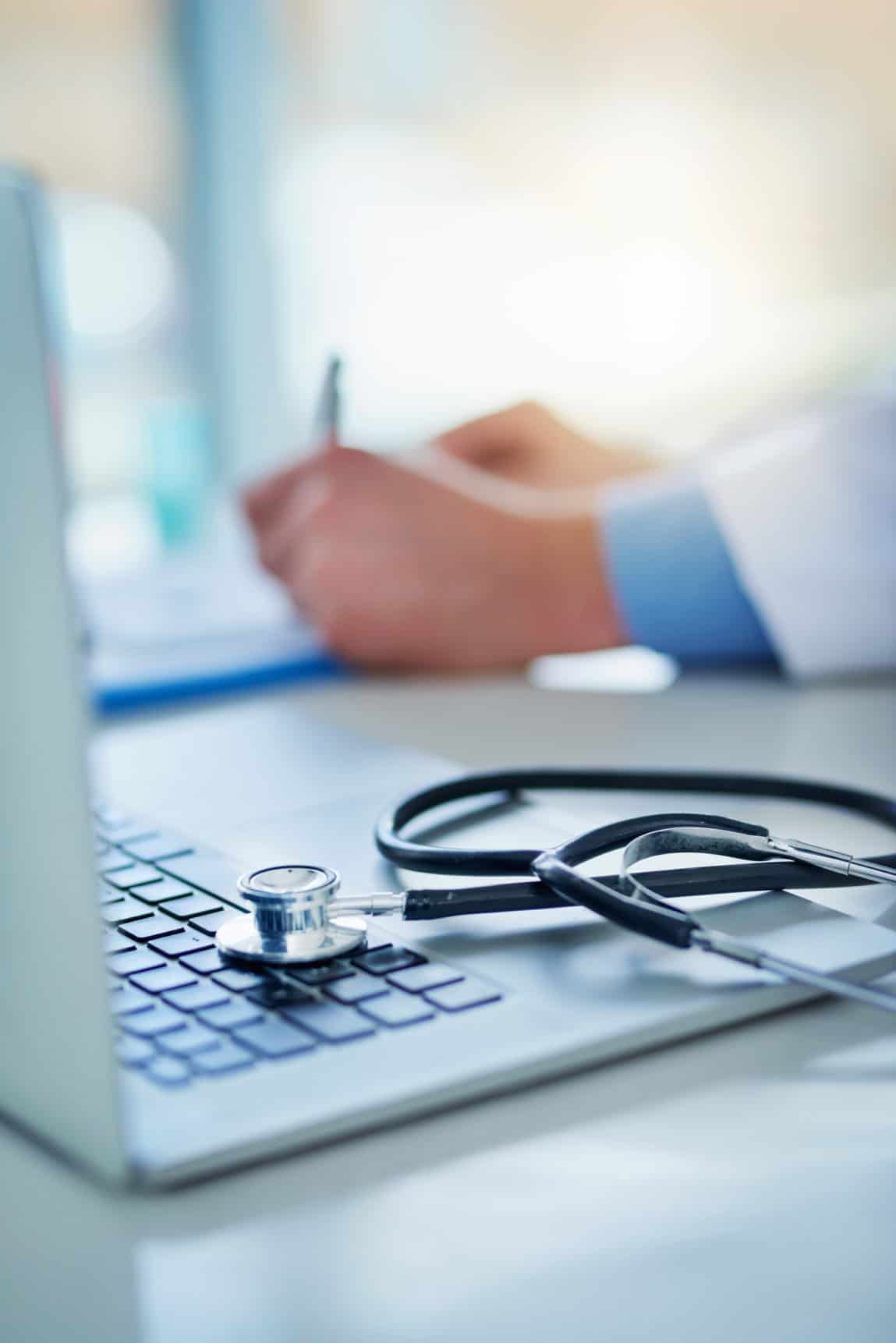 Closeup shot of a stethoscope resting on a laptop with an unrecognizable doctor working in the background