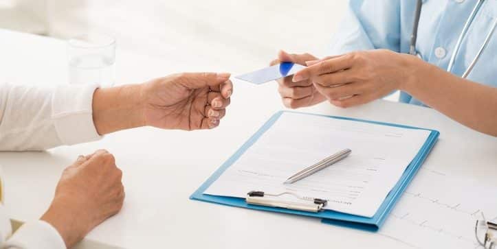 Hands of doctor giving health insurance card to senior patient