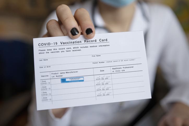 Close up of unrecognizable female doctor holding a COVID-19 Vaccination record card.
