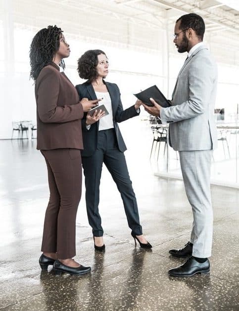 Commercial real estate: Business partners meeting onsite. Business man and women standing in modern office hallway, holding documents and digital devices, talking to each other. Partnership concept