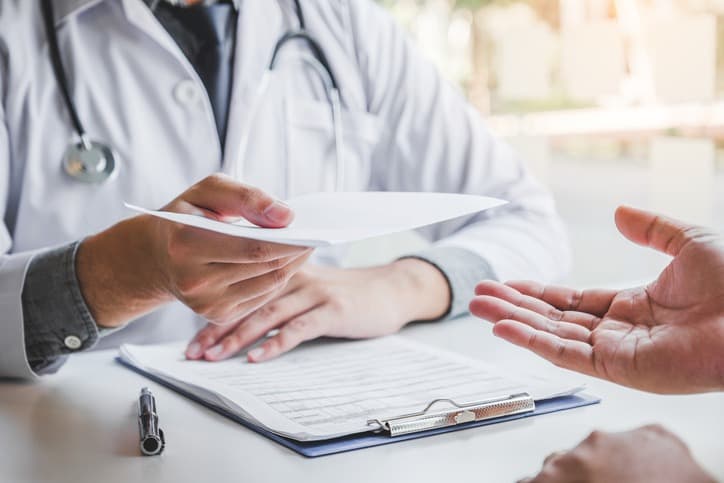 Payer Strategy in healthcare: DOcotr and patient exchanging health insurance information, interior shot of a doctor's office and desk